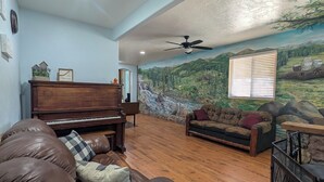 A living room with a piano, leather sofa, and a mural of a mountainous landscape.