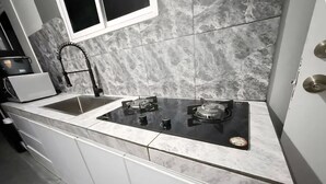 Une cuisine moderne avec une plaque de cuisson noire, des armoires blanches et un dosseret en marbre.