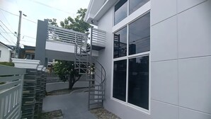 Un bâtiment moderne doté d’un escalier en métal menant à un balcon, entouré d’une clôture blanche et bordé d’un chemin recouvert de gravier.