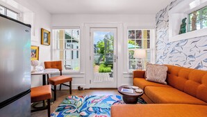 A compact living space with a kitchen, dining area, and seating area. It features a large window with a view of the outside, a patterned rug, and a decorative wall with a dolphin motif. - Tiny House Living + Parking | Near West End Beach (Provincetown)