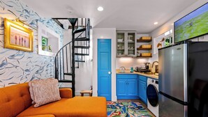 A compact living space with a sofa, a patterned rug, a washing machine, and a kitchen area with cabinets and a refrigerator. - Tiny House Living + Parking | Near West End Beach (Provincetown)