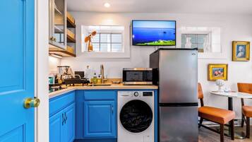 A compact kitchen with blue cabinets, a washing machine, a refrigerator, a microwave, and a television on the wall.