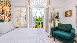 A bedroom with a bed, a green armchair, and a balcony with a view. - Tiny House Living + Parking | Near West End Beach (Provincetown)