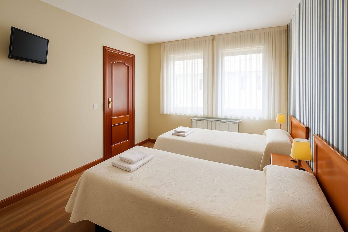 A hotel room with two beds, a television mounted on the wall, a door, and a window with sheer curtains.