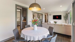 A modern dining area with a round table, chairs, a vase of flowers, and a pendant light.
