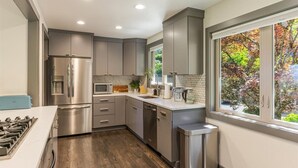 A modern kitchen with stainless steel appliances, a wooden countertop, and a view of autumn foliage through a window.