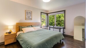 A bedroom with a bed, nightstand, lamp, artwork, windows, and a door.