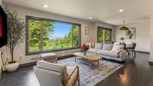 A spacious living room with a large window, a sofa, a coffee table, and a dining area.