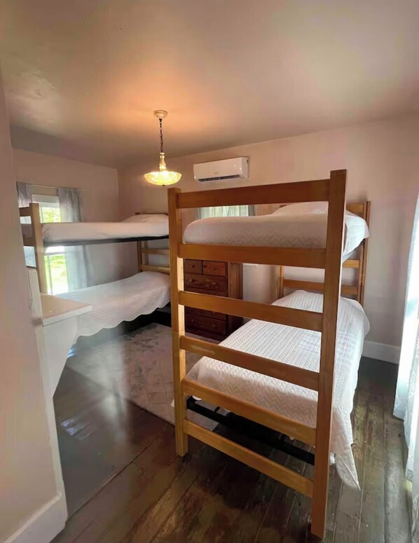 Habitación con literas, una escalera de madera, una lámpara colgante y una ventana con cortinas.