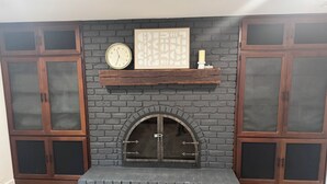 Una chimenea con revestimiento de ladrillo, un reloj y una obra de arte enmarcada encima.