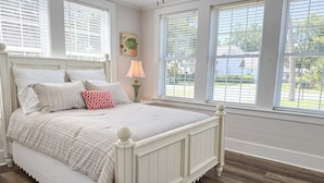 Un dormitorio con una cama blanca, una lámpara y ventanas amplias.