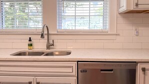 Una cocina con un lavamanos de acero inoxidable, lavavajillas y armarios blancos.