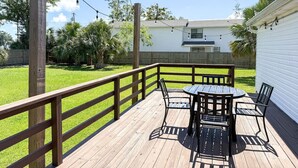 Una terraza de madera con una mesa y sillas, rodeada por una barandilla de madera, y luces colgantes.