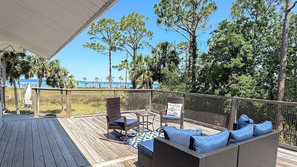 A covered outdoor deck with a wicker sofa and chairs, a small table, and a view of the ocean and trees. - Scalloper`s Dream House (Port St. Joe)