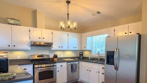 A modern kitchen with stainless steel appliances, white cabinetry, and a wooden floor. - Scalloper`s Dream House (Port St. Joe)