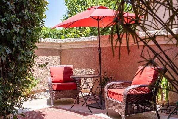 An outdoor patio with wicker furniture, a red umbrella, and a brick floor. - Desert Dream Getaway (Palm Desert)
