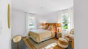 Um quarto com uma cama, duas mesas de cabeceira, uma cadeira, um espelho e uma janela.