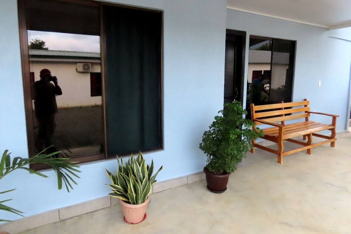 A building exterior with a large window, a wooden bench, and potted plants.