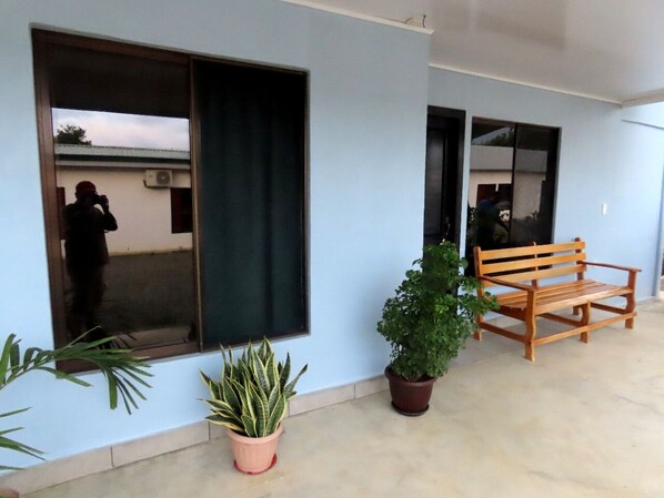 Fachada de un edificio con un ventanal grande, un banco de madera y plantas en macetas.