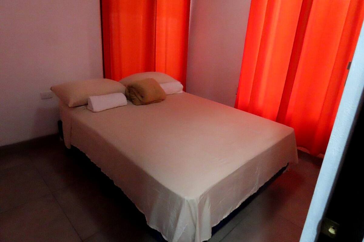A single-bed room with a beige bedspread, two pillows, and a single blanket.
