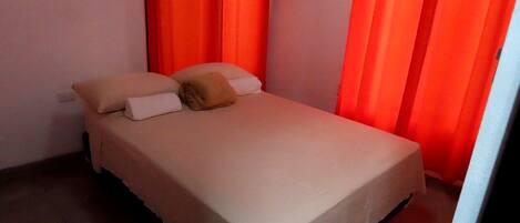 A single-bed room with a beige bedspread, two pillows, and a single blanket.