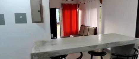 A kitchen with a marble countertop, four black bar stools, a ceiling fan, and a red curtain.