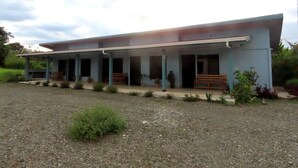 A two-story building with a covered porch and a gravel driveway. - Villas Arena y Sol (Puerto Jiménez)