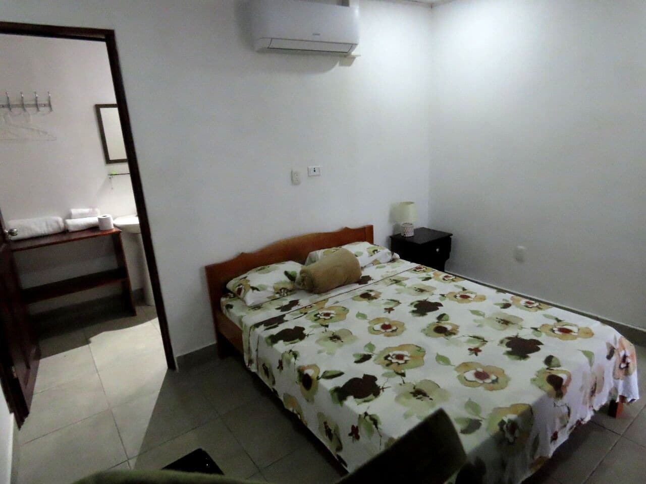 Un dormitorio con cama, mesita de noche, armario de madera y aire acondicionado en la pared.