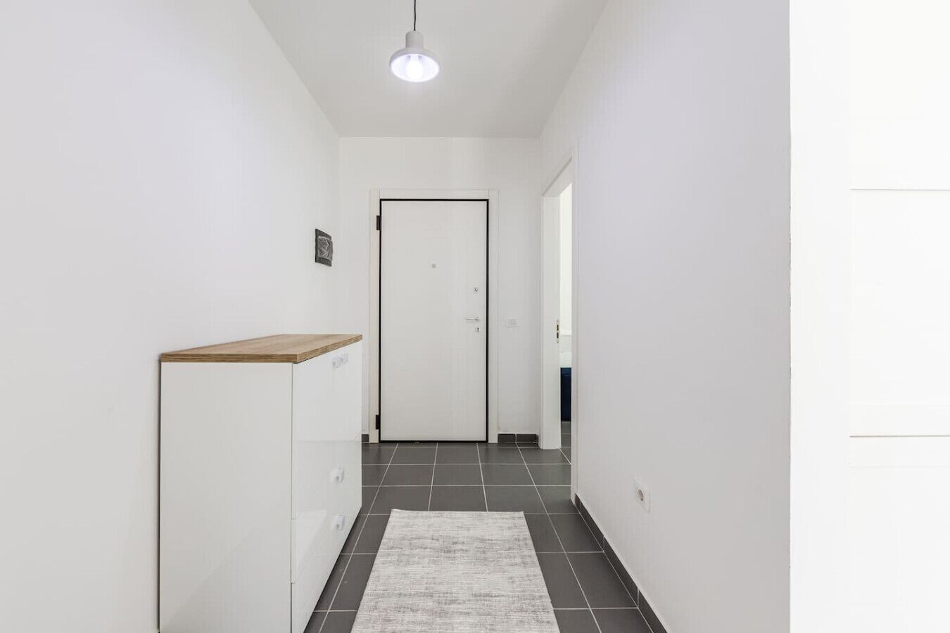 Um corredor com uma porta branca, uma pequena estante de madeira e um tapete no chão.