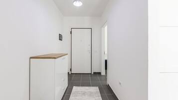 Um corredor com uma porta branca, uma pequena estante de madeira e um tapete no chão.
