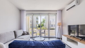 A modern living room with a sofa, a TV on a stand, and a balcony with outdoor furniture. - Talea Holiday Apartments | 1 by PikHost (Tale)