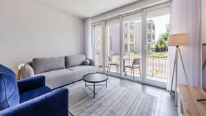 A modern living room with a grey sofa, a blue armchair, a small round table, and a floor lamp. - Talea Holiday Apartments | 1 by PikHost (Tale)
