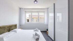 Quarto de hotel moderno com uma cama grande, cabeceira, janela com cortinas e vista para edifícios.