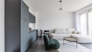Uma sala de estar moderna com um sofá cinzento, uma mesa de centro redonda e uma poltrona verde-escuro.