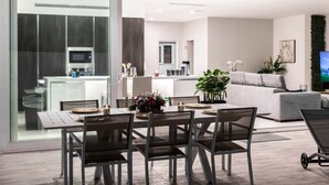 Una sala de estar moderna con un sofá gris, un comedor con una mesa lista para dos personas, y una cocina al fondo.