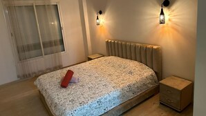 A bedroom with a bed, a nightstand, a window with curtains, and two wall-mounted lights.