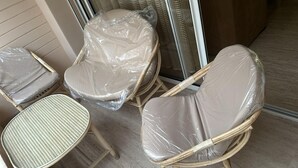 Three wicker chairs with plastic covers, a wicker table, and a glass door.