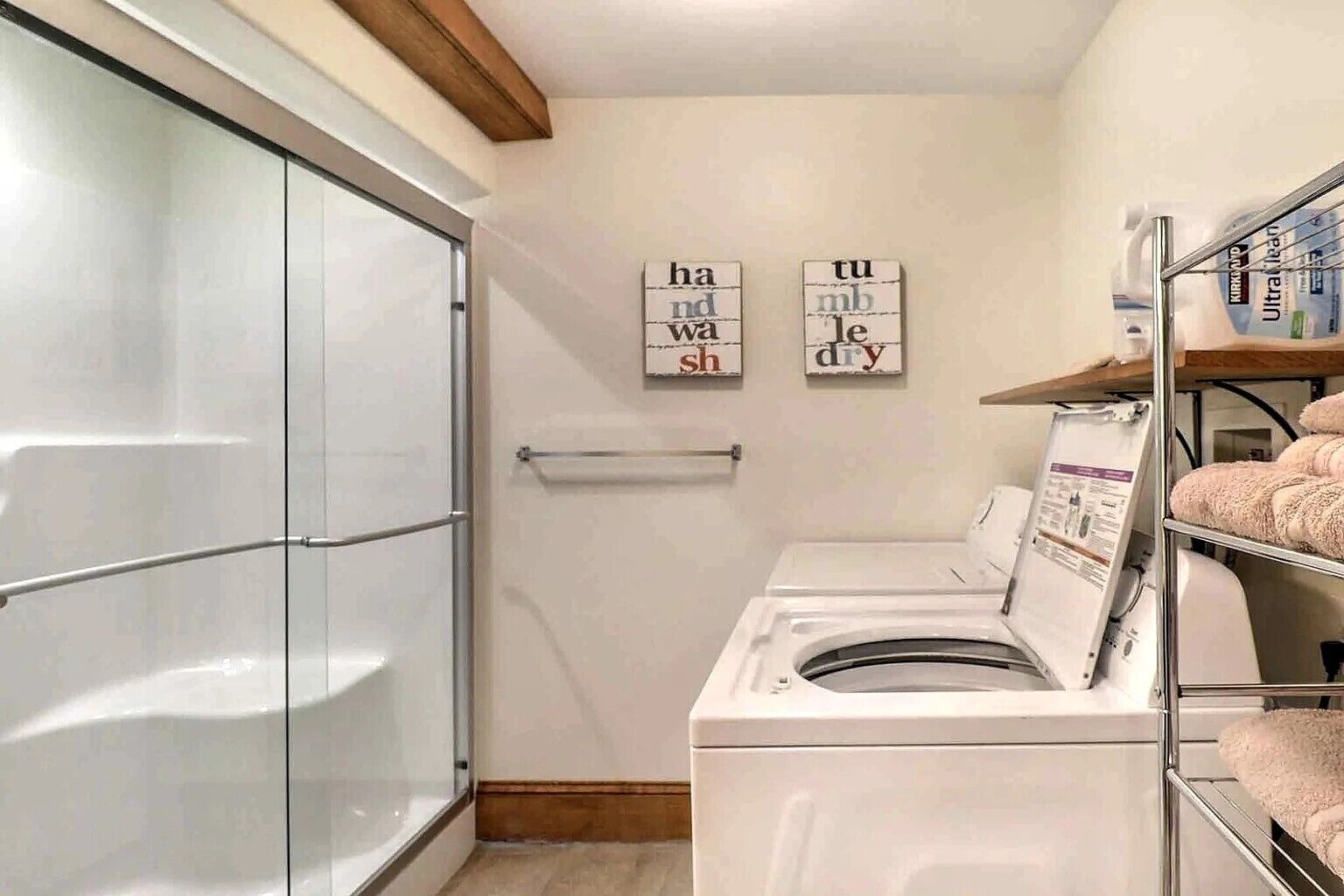 A laundry room with a glass shower enclosure, two wall-mounted washing machines, and a towel rack.