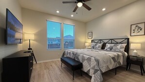 Ein Schlafzimmer mit Bett, Deckenventilator, Fernseher und einem Fenster mit Jalousien.