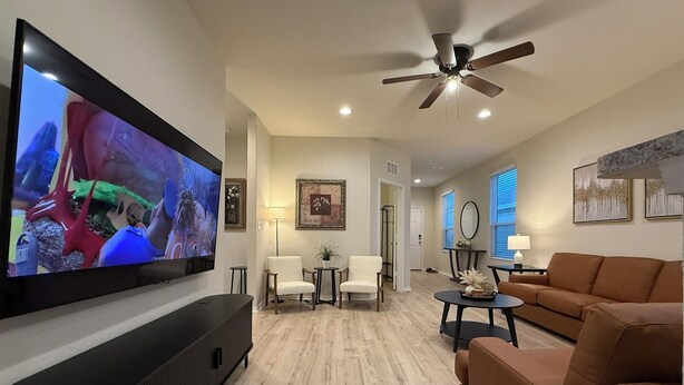 Ein modernes Wohnzimmer mit Flachbildfernseher, Deckenventilator und braunem Sofa.