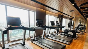 Une salle de sport équipée de tapis de course, de vélos d’exercice et offrant une vue sur la ville.