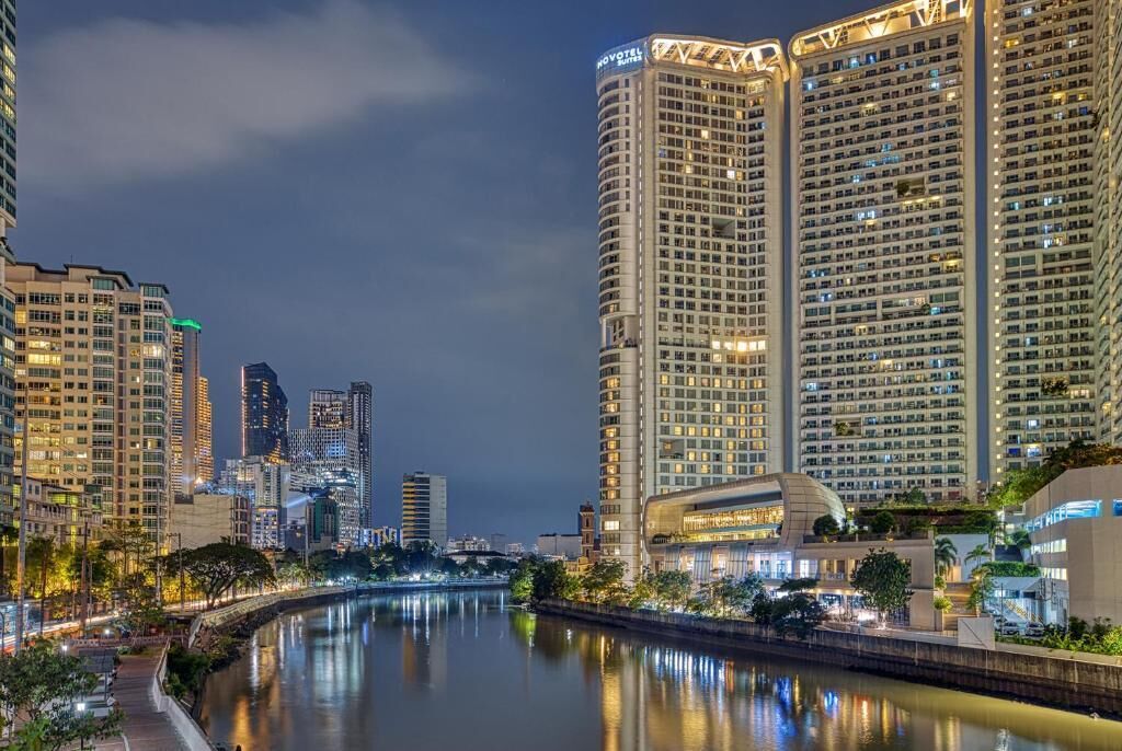 Un hotel de gran altura con varios pisos, un río en primer plano y otros edificios al fondo.
