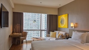 Une chambre d’hôtel avec un grand lit, un bureau, une chaise, un canapé et une vue sur un immeuble de grande hauteur.