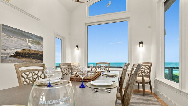 A dining area with a view of the ocean, featuring a table set for four with chairs, a painting on the wall, and a large window. - Peaceful Coastal Estate | Beach Access + Sunrises (Palm Coast)