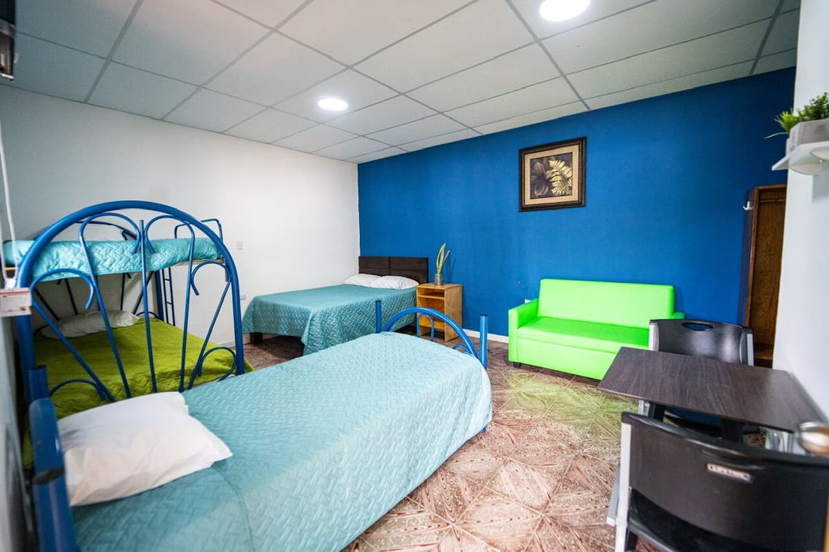 A room with two beds, a green sofa, a small table, and a TV.