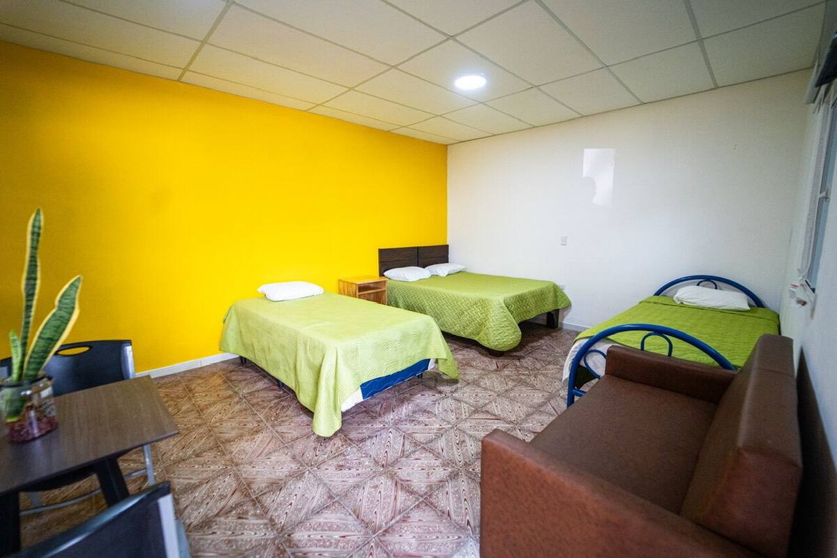 A room with three beds, a small table, and a chair.