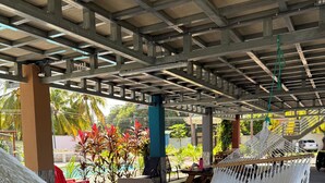 A covered outdoor seating area with white hammocks and a view of palm trees.