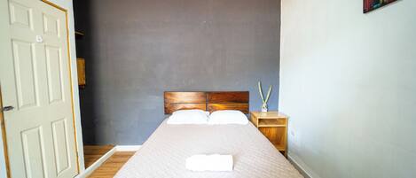 Una camera da letto con un letto, un comodino, una porta e una parete con un quadro.