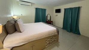 A bedroom with a bed, a dresser, an air conditioner, a mirror, and teal curtains. - Marvin's Apartment - 46 (Sint Michiel)