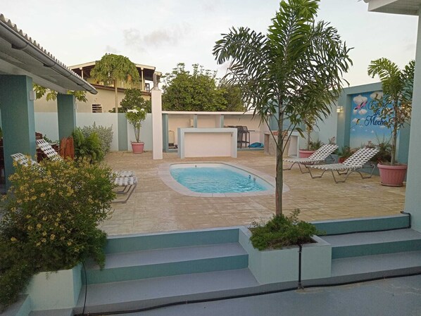 Une piscine avec des chaises longues, un petit escalier et des plantes en pot.